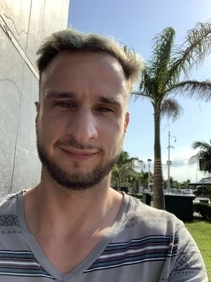 The author, hair dyed blue, standing in front of a palm tree, squinting due to the tropical sun.