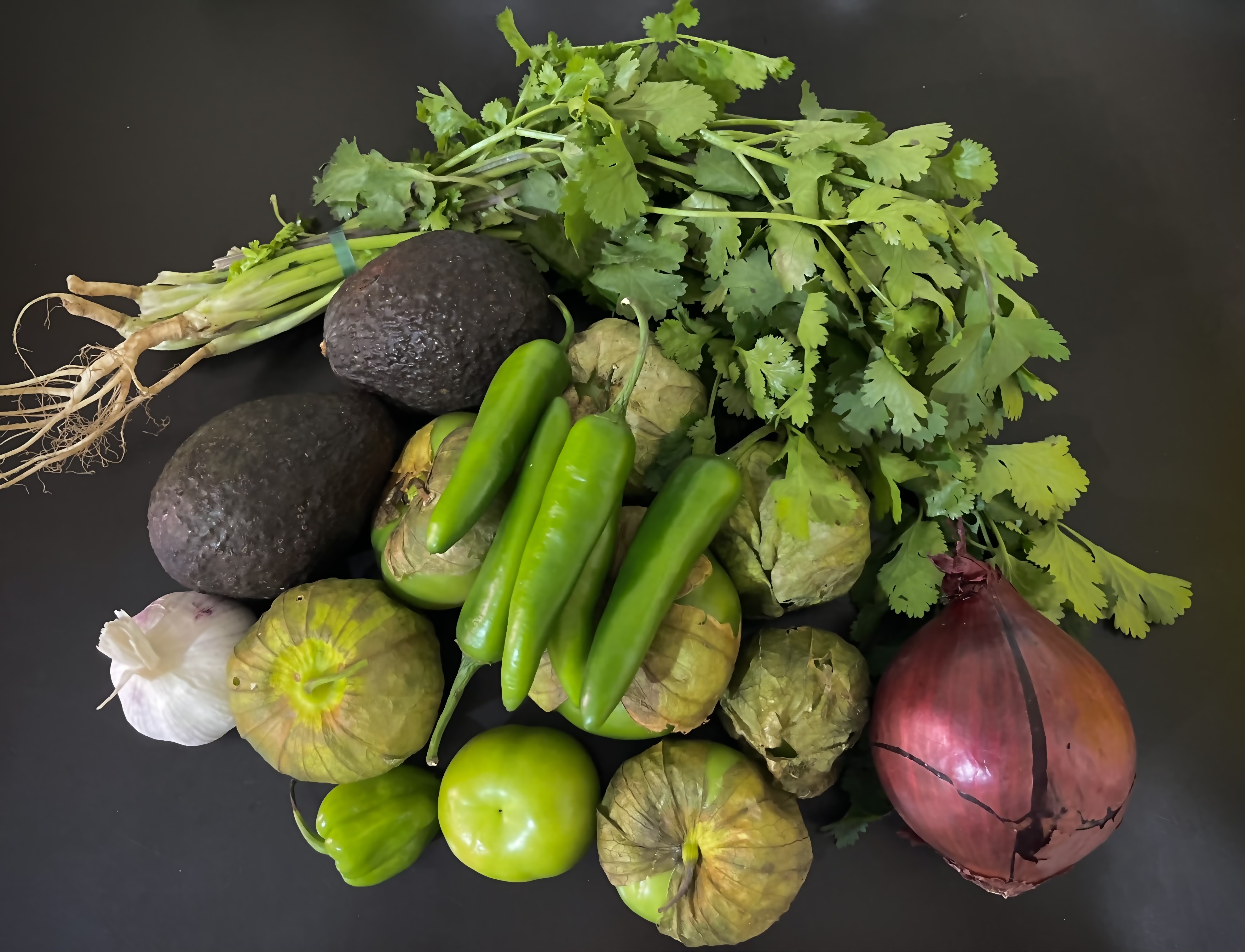 The ingredients for making salsa verde spread out on the table. The green tomatoes are fresh still with their leaves attached!